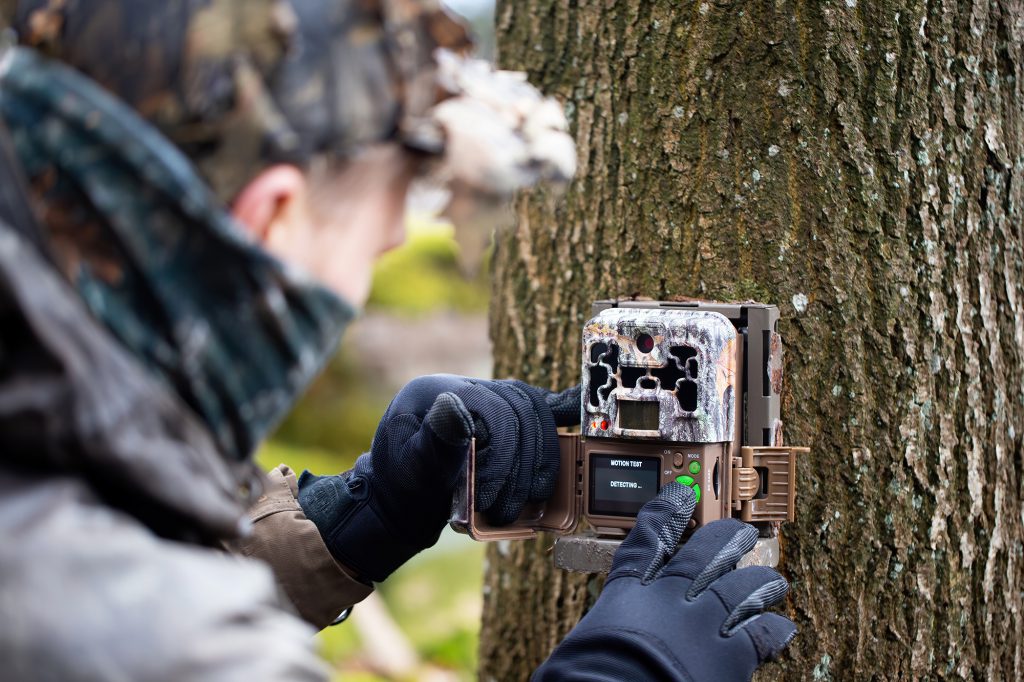 person setting up a trail cam on a tree