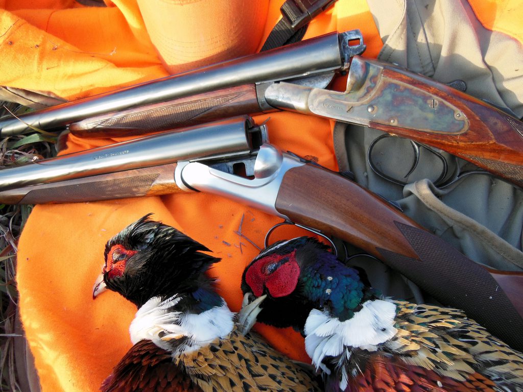 two side-by-side shotguns with dead pheasants
