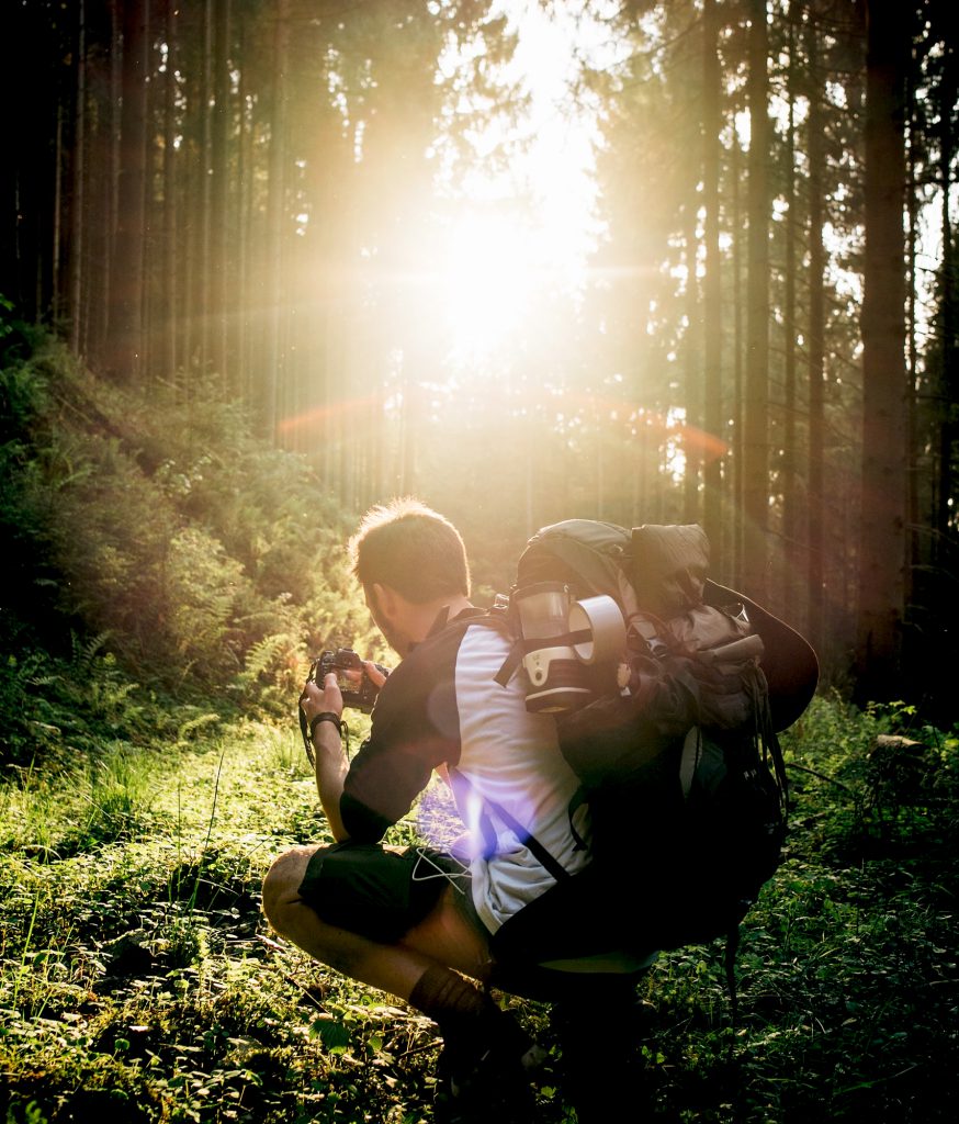 backpacker crouching in woods with camera