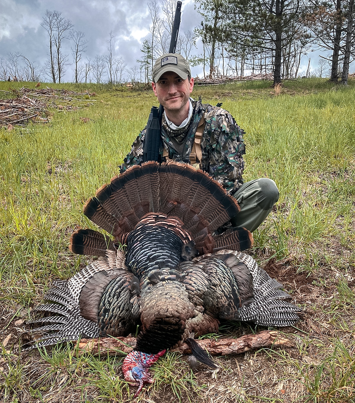 Hunter in a hunting ghillie suit posing with his turkey