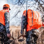 Hunters wearing orange drag deer out of the woods