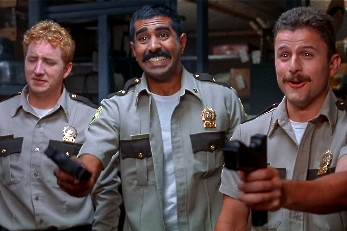Foster (Paul Soter), Thorny (Jay Chandrasekhar), and MacIntyre (Steve Lemme) eagerly await Captain O’Hagen’s pistol-whipping in the 2001 movie Super Troopers.